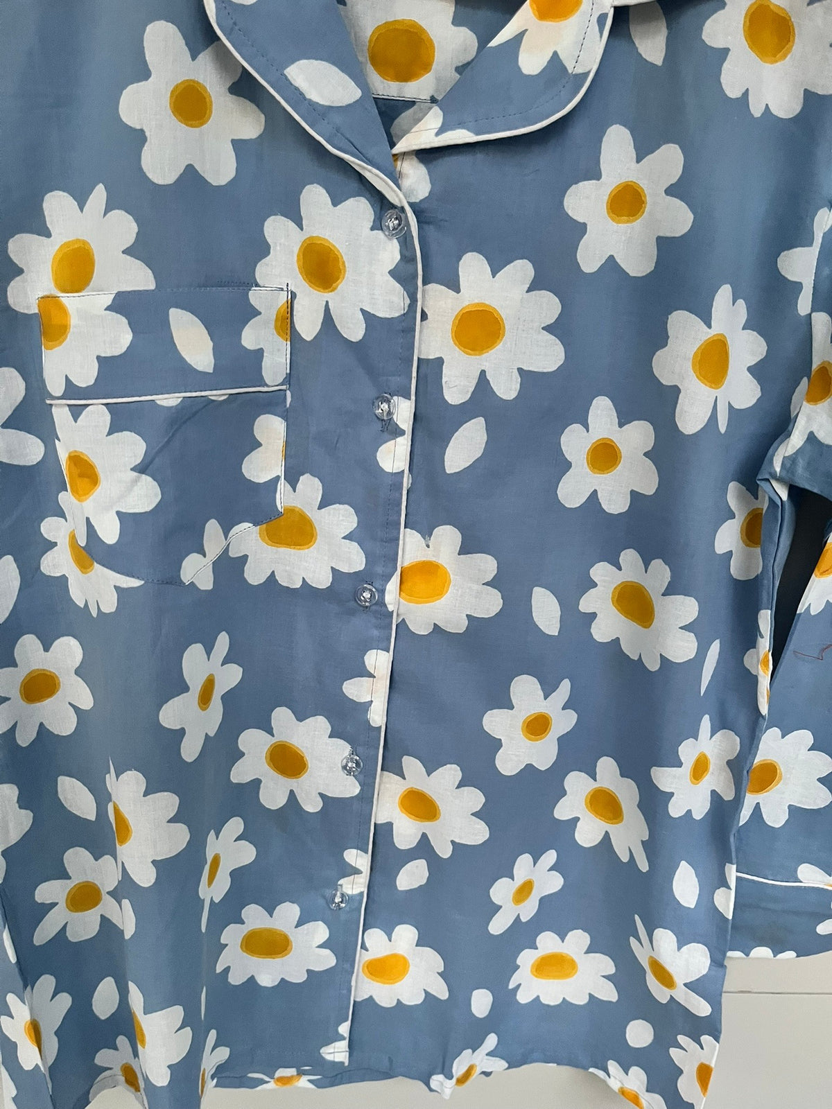 Wild Lotus UK blue cotton pyjama top with white daisy print, revere collar, chest pocket, and white piping detail.