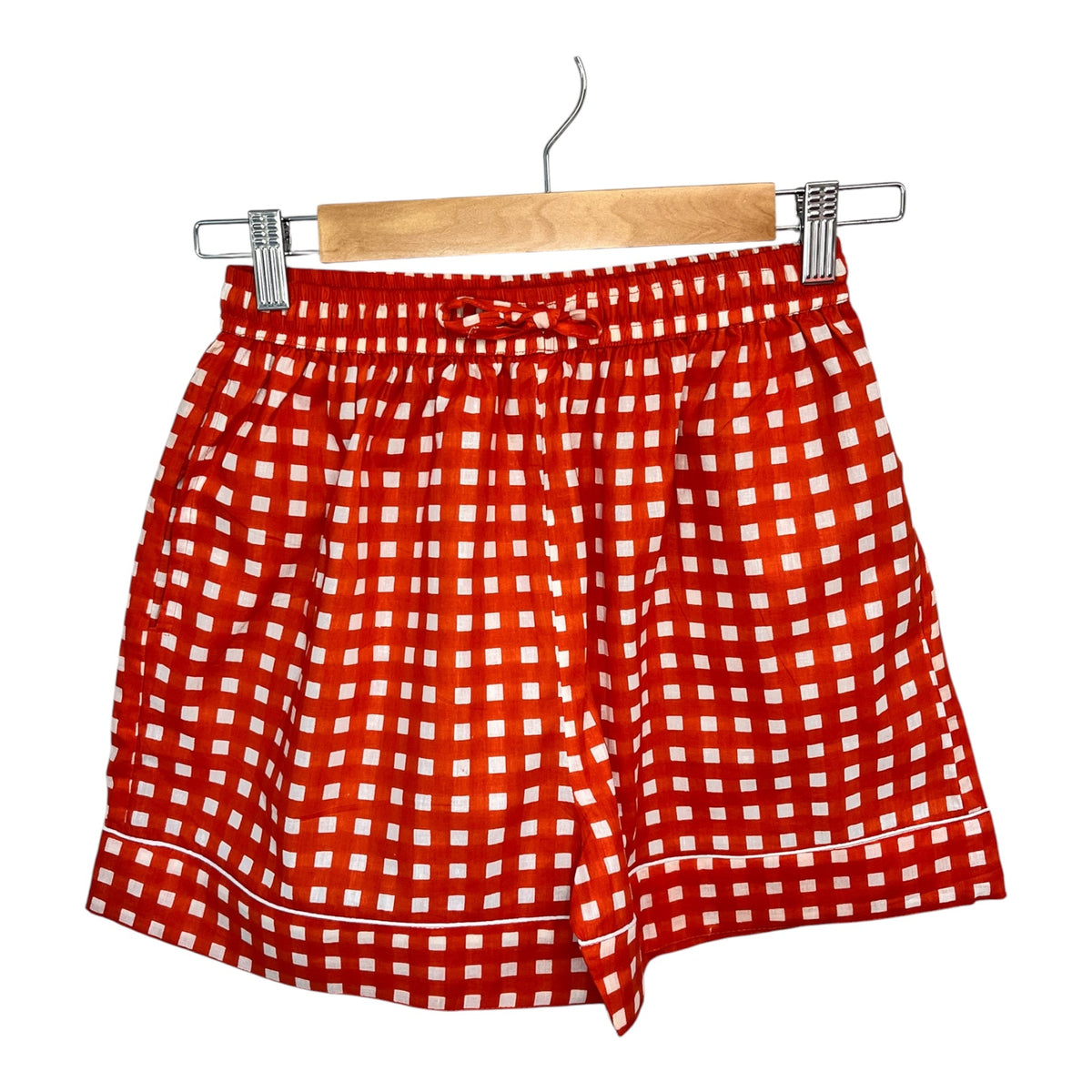 Wild Lotus UK orange and white gingham cotton pyjama shorts with white piping detail hanging on a wooden hanger