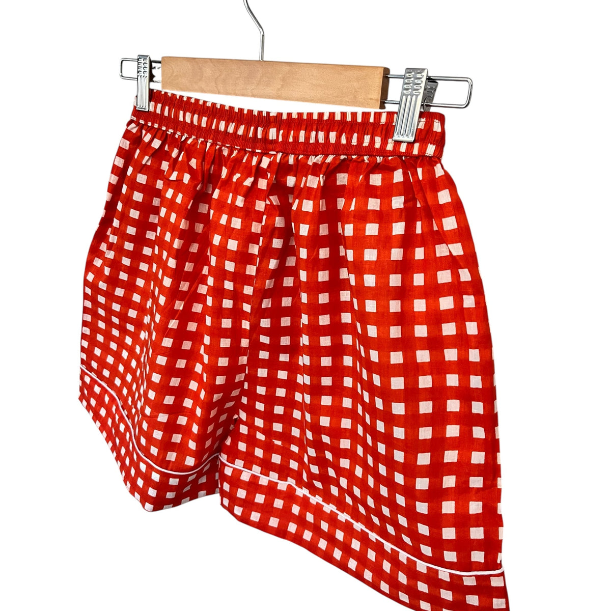 Wild Lotus UK orange and white gingham cotton pyjama shorts with white piping detail hanging on a wooden hanger